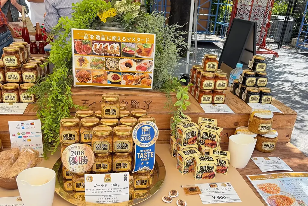 太陽のマルシェに出店していた「ゴールデンマスタード」の店頭。2018年優勝や2019年最高金賞の盾と共に瓶詰めが並んでいる様子。