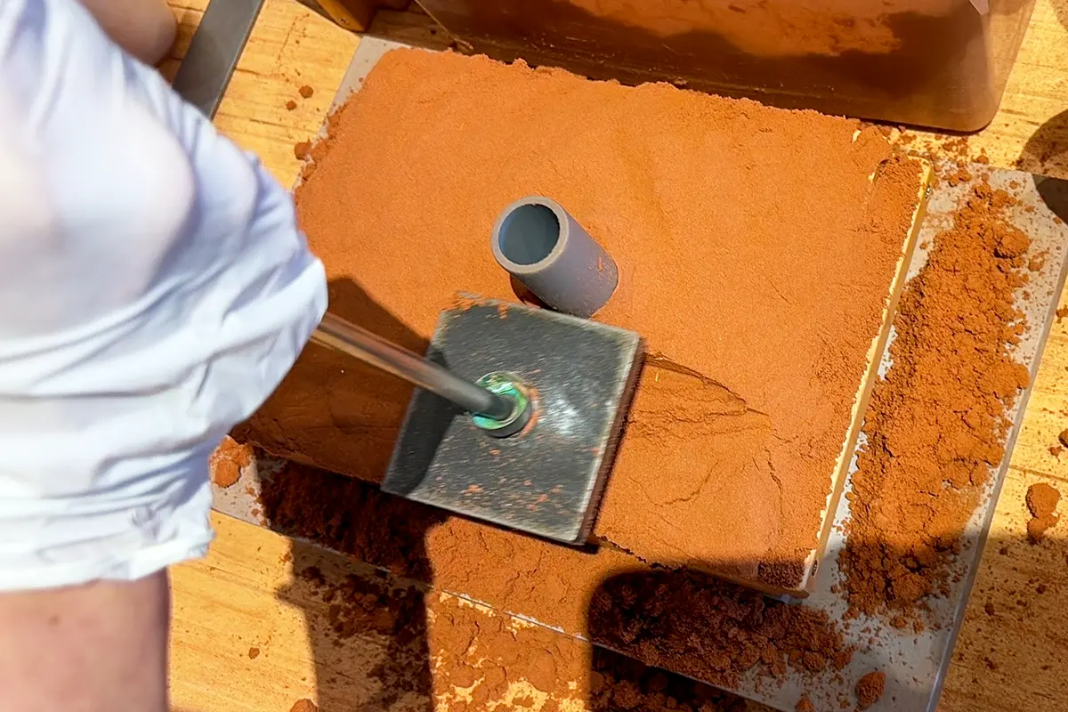 スタンプ状の道具で砂の表面を平らに整える工程