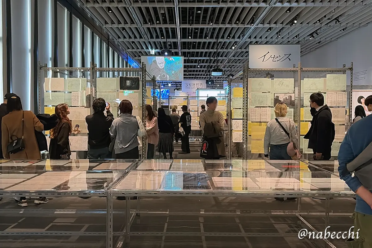 多くの来場者が、金属ラックに並べられた膨大な数の手書き原画を鑑賞している展示エリアの全景