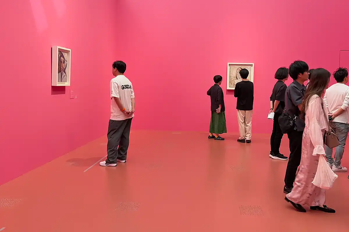 床から壁まで全面がビビッドなピンク色で統一された展示室で、熱心にピカソの絵画を鑑賞する人々。空間演出のカラーグラフィックが映える様子