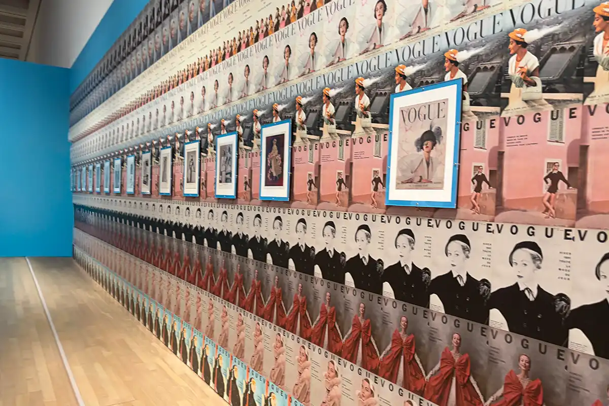 雑誌『VOGUE(ヴォーグ)』のレトロな表紙が壁一面に敷き詰められた、インパクトのあるおしゃれな展示空間。青いアクセント壁と額装された表紙が並ぶ様子