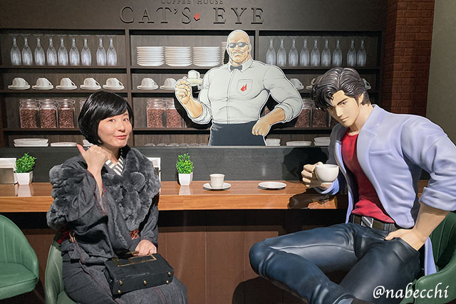 喫茶キャッツアイのセットで、黒デニム着物姿の筆者が冴羽獠と海坊主の等身大パネルと並んで座る3ショット